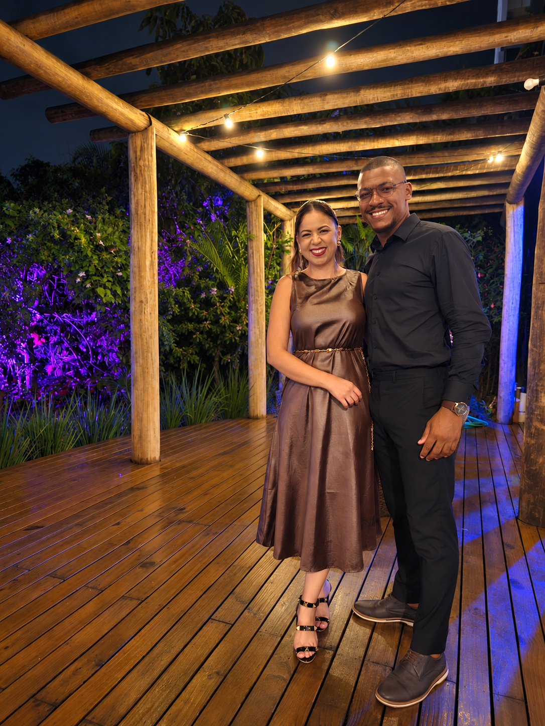 Casal sob uma pérgola de madeira iluminada